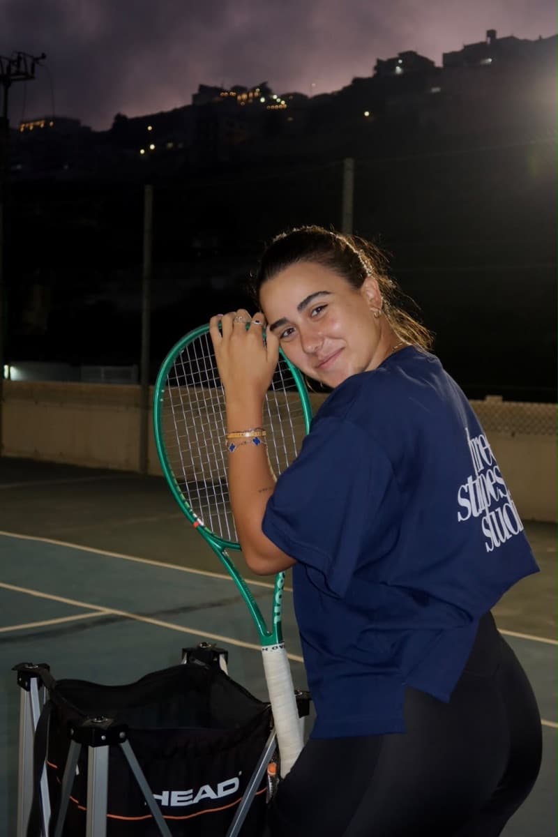 Mina on a floodlit court at night, leaning on her racquet